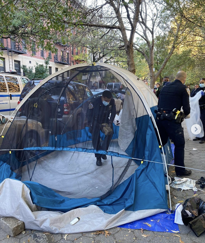 NYPD officer entering an empty tent on the side of the road.
