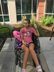 Avery in her wheelchair, smiling and making a peace sign.