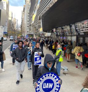 Protestors hold up signs for the adjunct professor union, UAW, marching in front of the New School main campus building on Fifth Avenue.