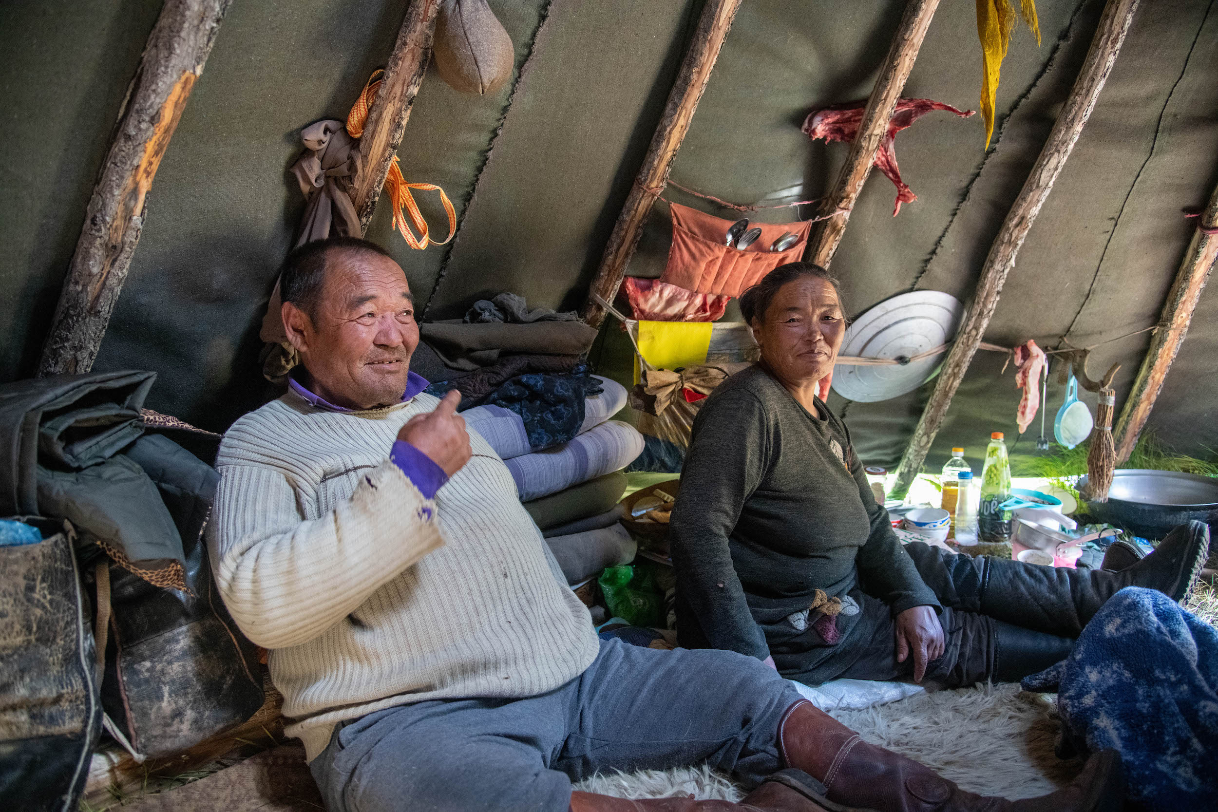 Two Tuvan reindeer herders, Mandah and Oyunaa, sit inside a tent made of wood posts and tarps.