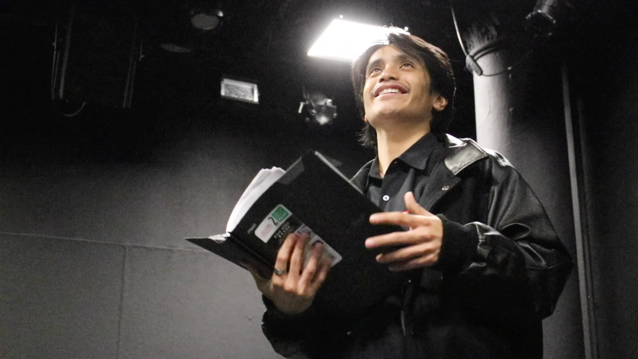 NYU Tisch drama student Brandon Bautista stands in a film studio holding a script