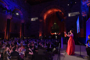 Woman in a red gown addressing a crowd at the Endometriosis Foundation of America's 11th Annual Blossom Ball. Image by Bryan Bedder/Getty Images