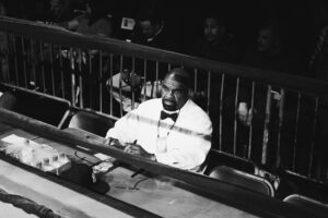 A Battle of the Badges boxing judge sitting behind the rink wearing a white tux and black bow tie.