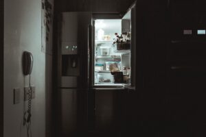 An open fridge in a dark apartment at night.