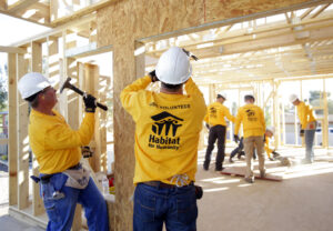 Volunteers work at a Habitat for Humanity in construction with a hamer building a door frame