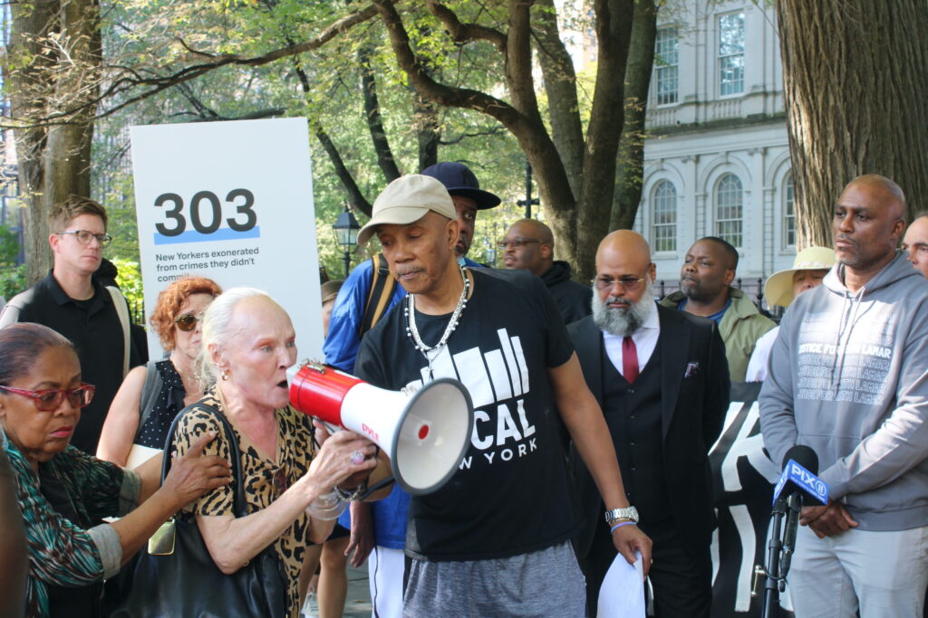 A woman is supported as she passionately speaks into a blow-horn in a crowd outside city hall.