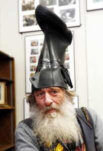 Vermin Supreme, a white man with a long white beard and an upside-down black boot on his head, poses for a picture.