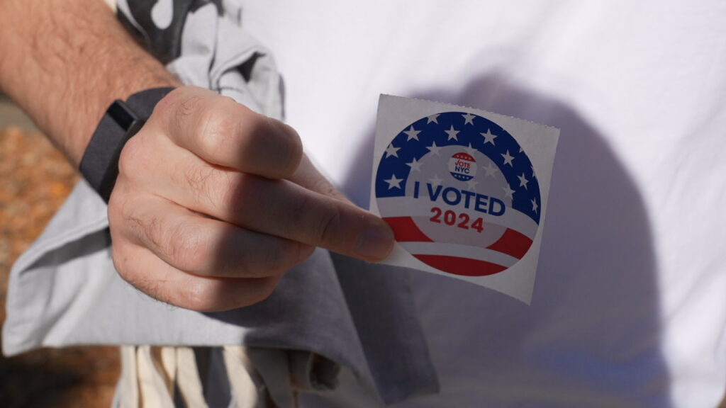 Close-up of a hand holding a 2024 "I Voted" sticker in New York City.