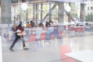 Multiple women seated at a table writing letters, seen through a reflective window in Manhattan.