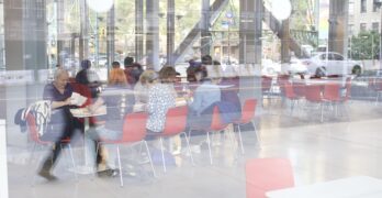 Multiple women seated at a table writing letters, seen through a reflective window in Manhattan.