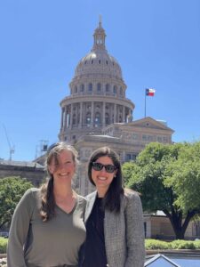 Morris and her lawyer Lauren Ice stand next to each other smiling in front of the Texas capitol building. Morris wears a gray top and her blonde hair is in a side ponytail. Ice wears a black top with a gray jacket. She has brown hair and is wearing sunglasses.