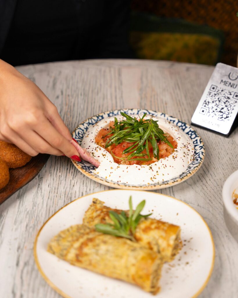 A plate of hummus and crepes beside a QR code for a restaurant menu